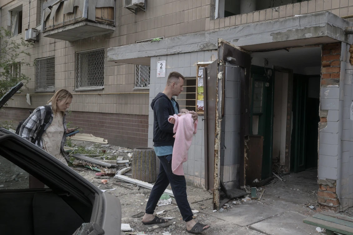 Пара з немовлям на руках заходить до пошкодженого будинку в Києві після ракетного удару, що спустошив житловий район.