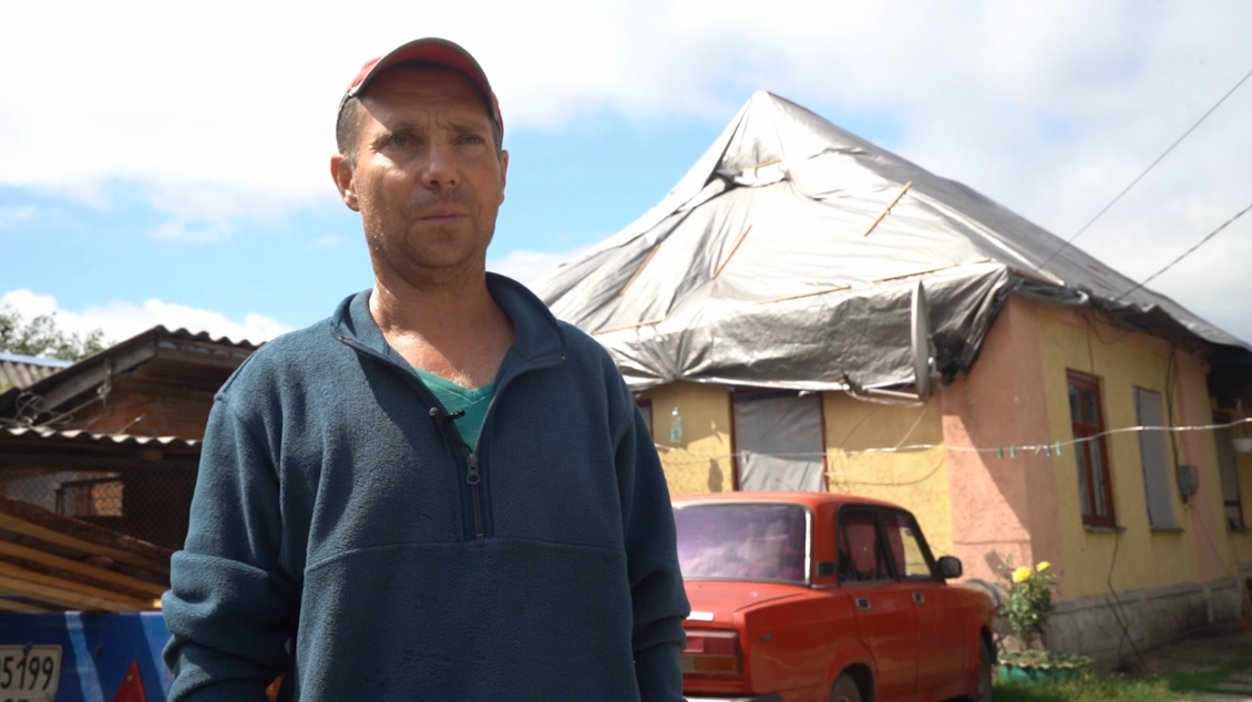 Oleksii in front of his damaged home 